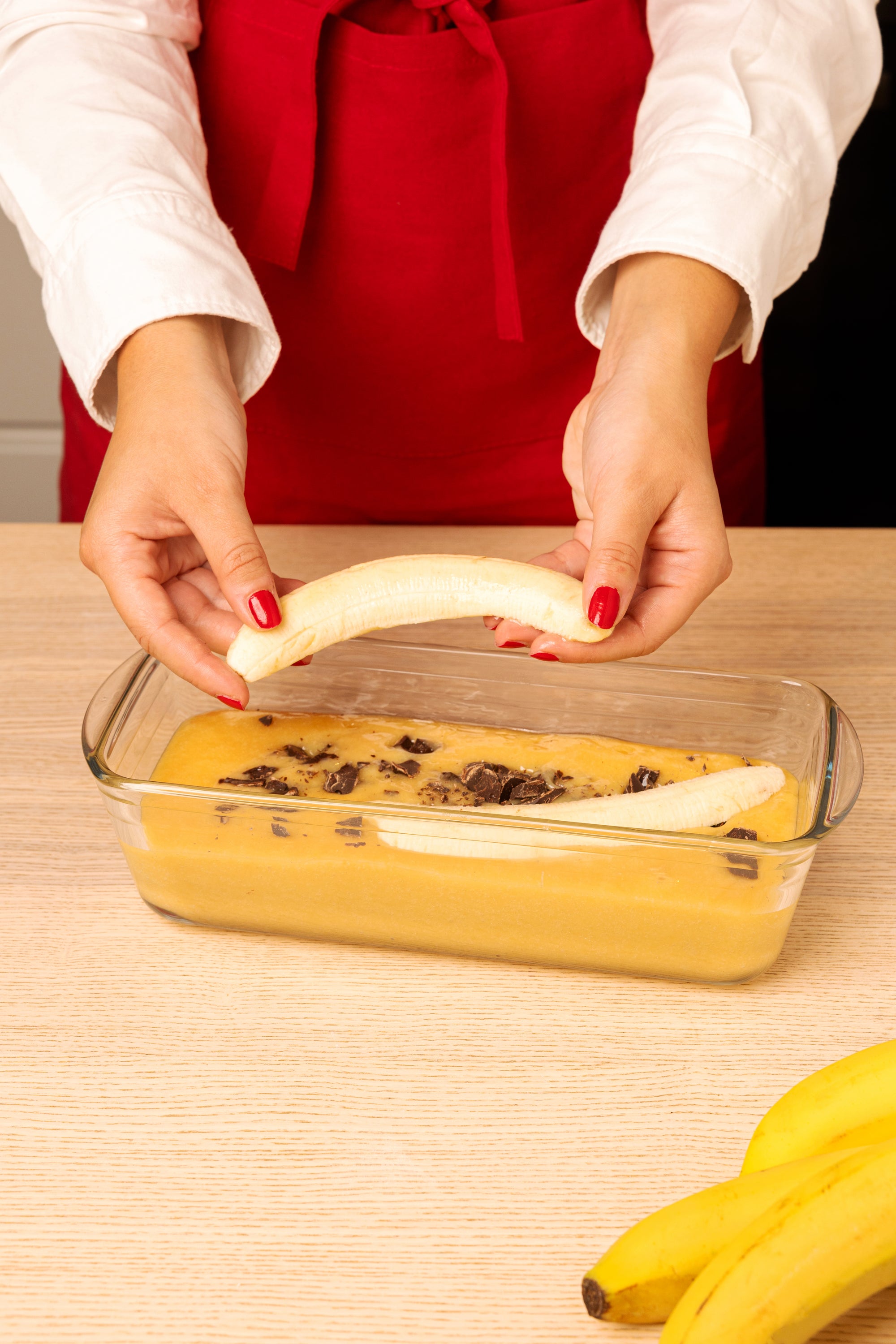 Person preparing a dessert with bananas in an ÔCuisine glass Loaf dish on a wooden table.